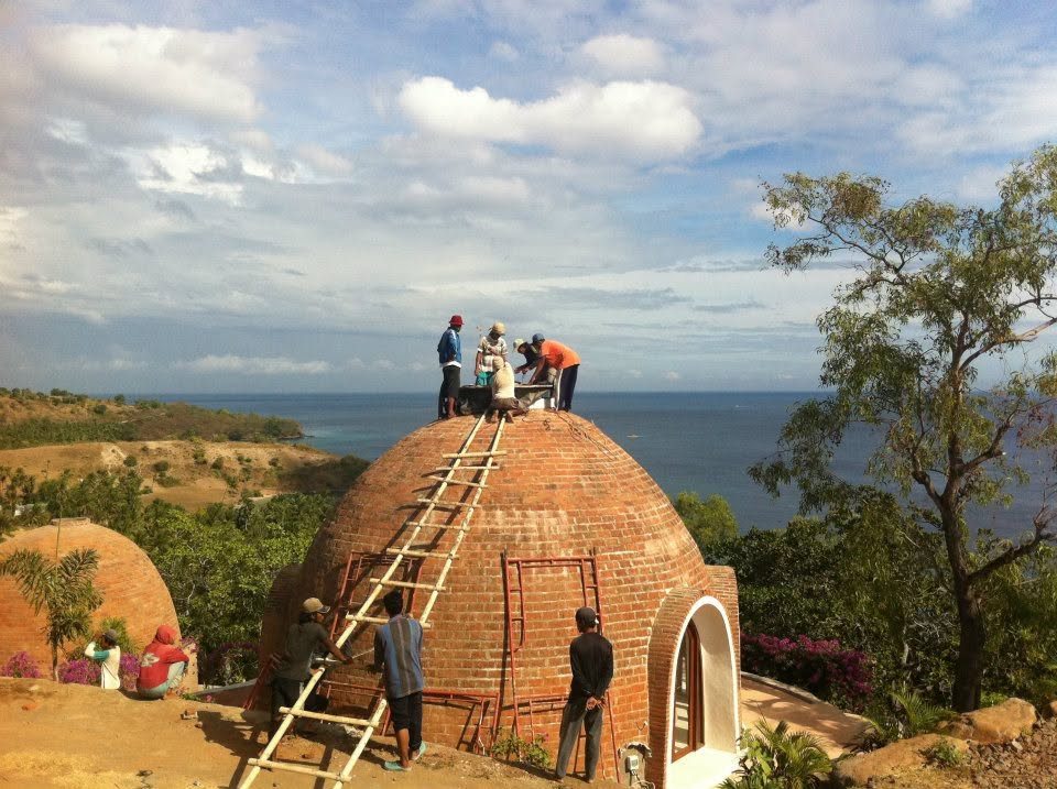 Building team on ladders against a brick dome above the ocean